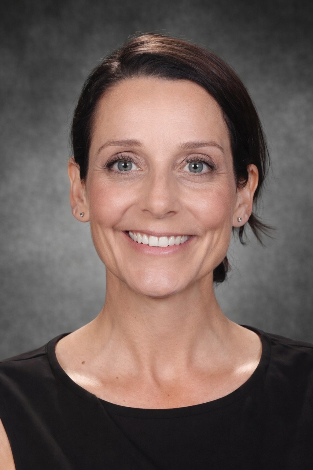 A white woman with short dark hair smiles, wearing a black top.